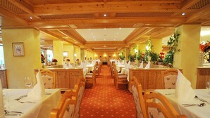 A long dining hall with wooden paneling and a red carpet. Tables are set with white tablecloths and silverware.