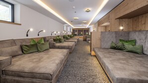 A modern interior with a row of sofas and benches along a central walkway, wooden paneling on the walls, and recessed lighting.