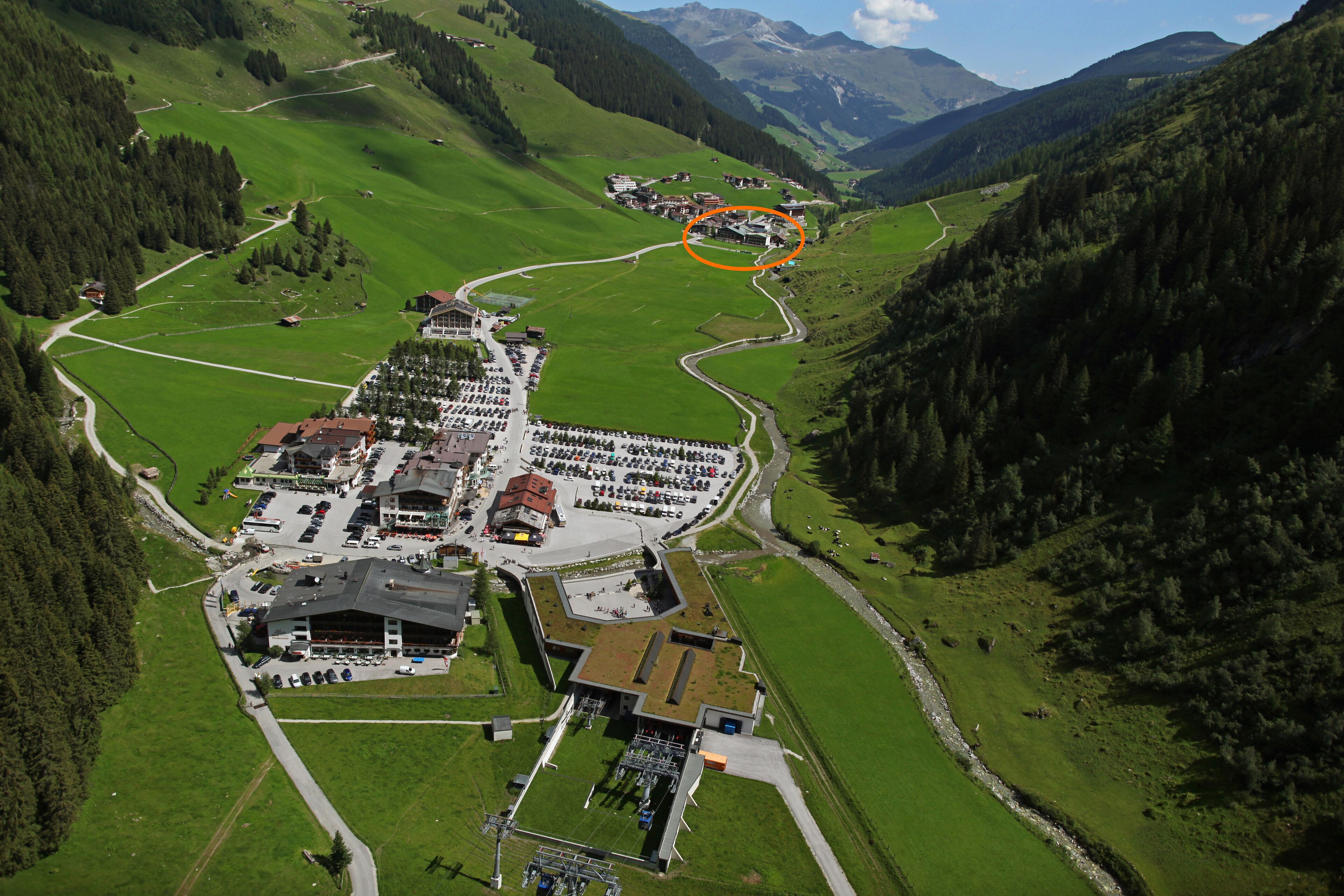 An aerial view of a hotel complex with multiple buildings, parking areas, and surrounding green hills.