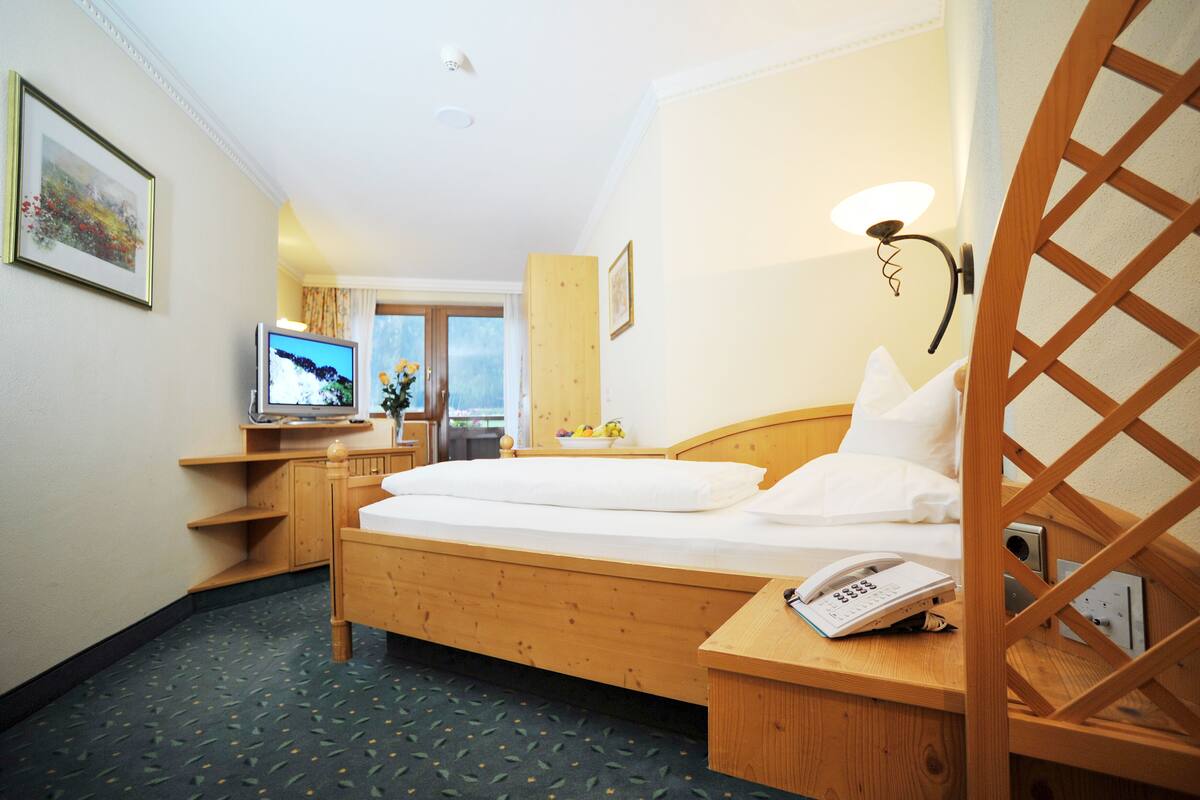 A hotel room with a wooden bed, a desk with a telephone, a television, and a window with a view.