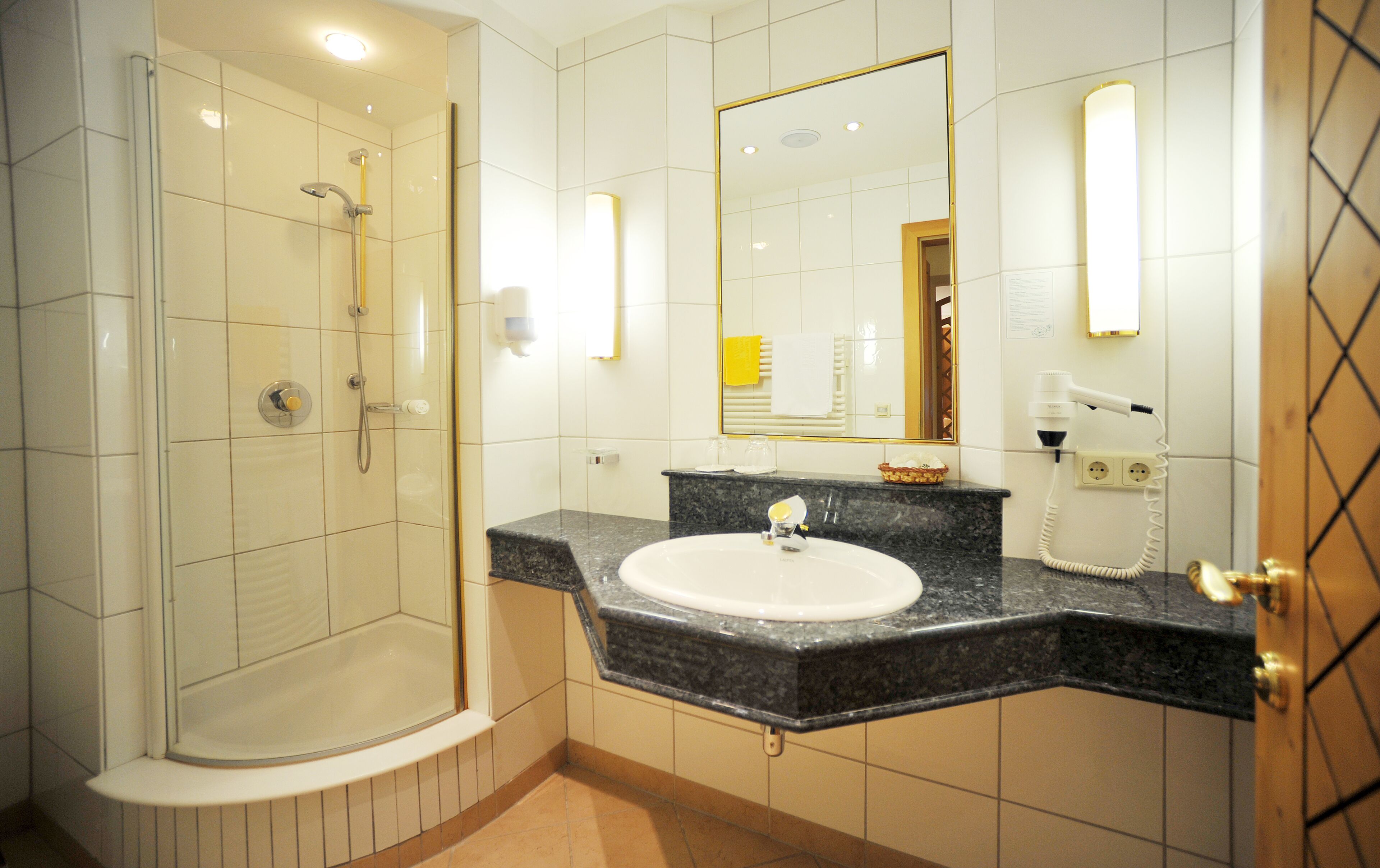 Une salle de bain moderne dotée d’une douche à parois de verre, d’un lavabo avec un plan de travail en marbre et d’un miroir avec éclairage intégré.