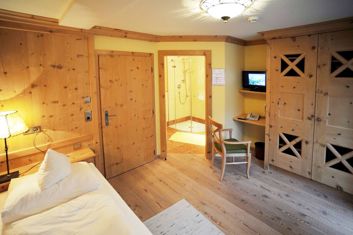 A hotel room with wooden walls, a bed, a chair, a desk with a computer, and a TV.
