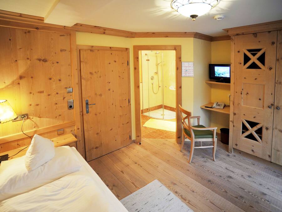 A hotel room with wooden walls, a bed, a chair, a desk with a computer, and a TV.