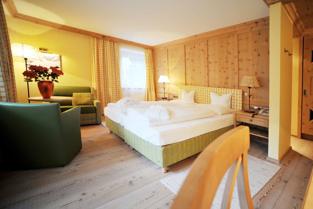 A hotel room with a large bed, a green armchair, a small table, and a wooden wardrobe.