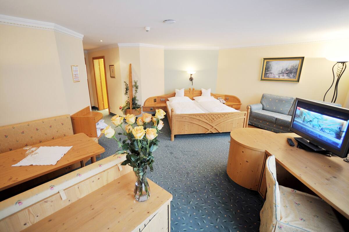 A hotel room with a wooden bed, a sofa, a desk with a television, and a vase of flowers.