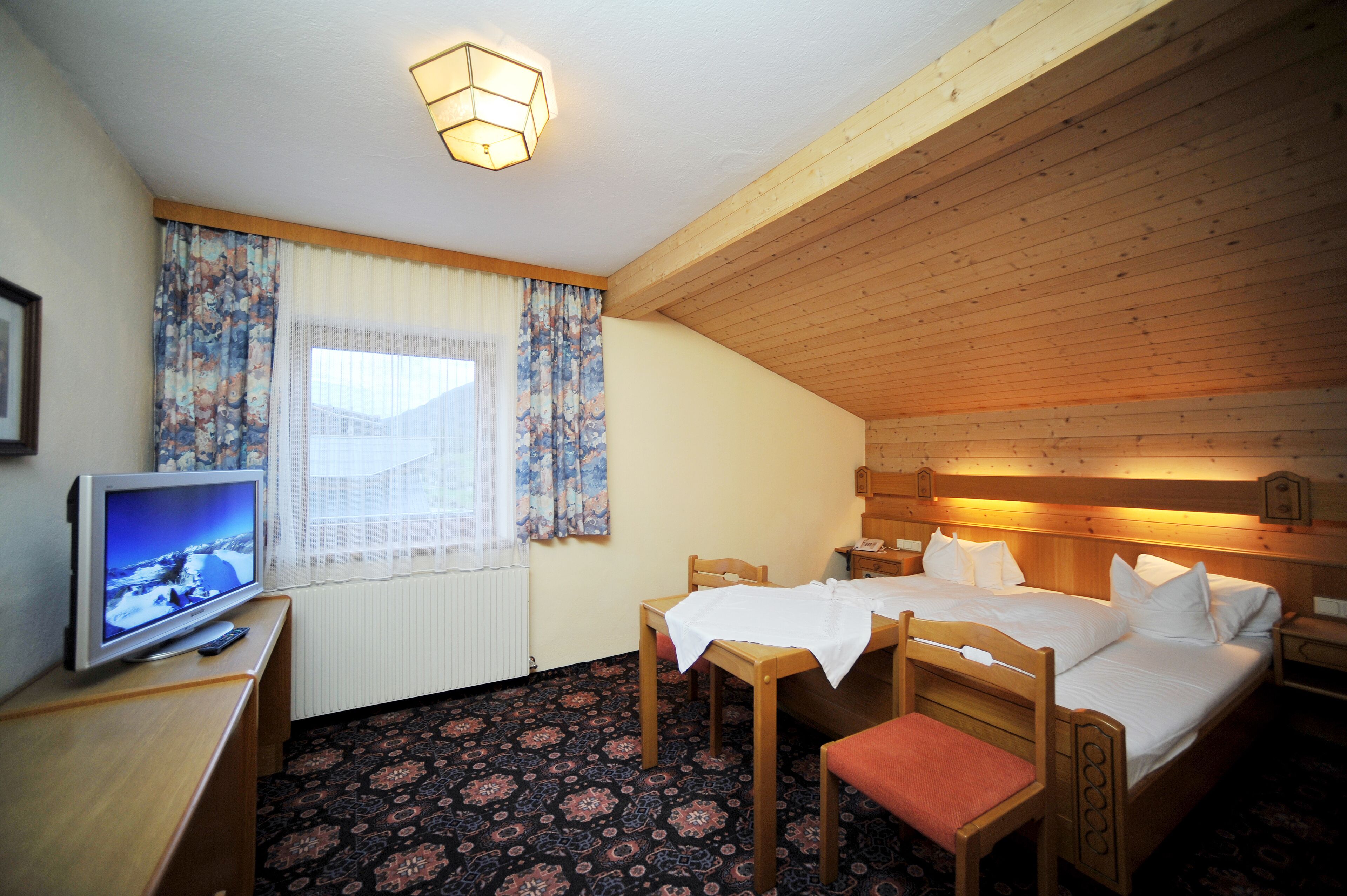 Een gezellige kamer met een bed, een bureau met een televisie en een raam met gordijnen.