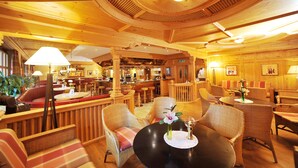 A wooden interior with round tables and wicker chairs, a bar area, and a seating section with cushioned benches.