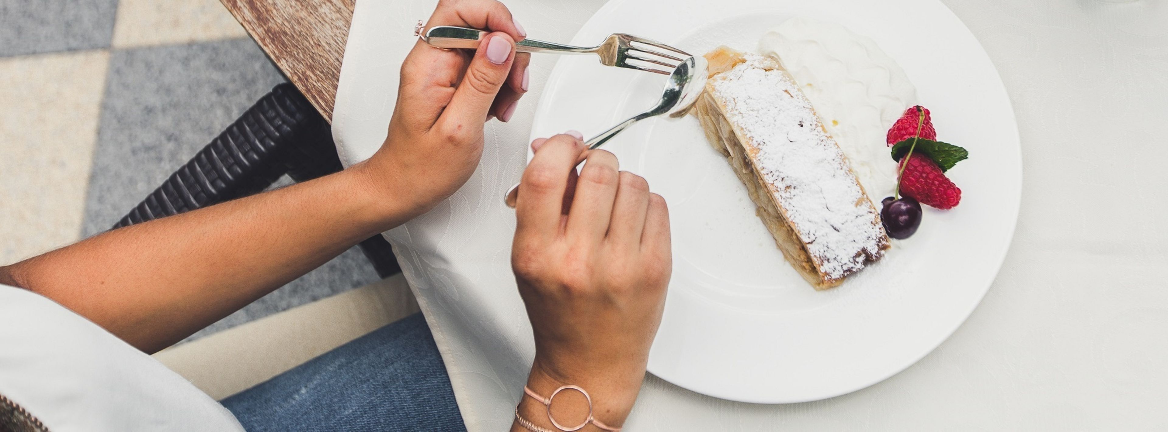A person using a fork to eat a dessert with strawberries and a cherry on a white plate.