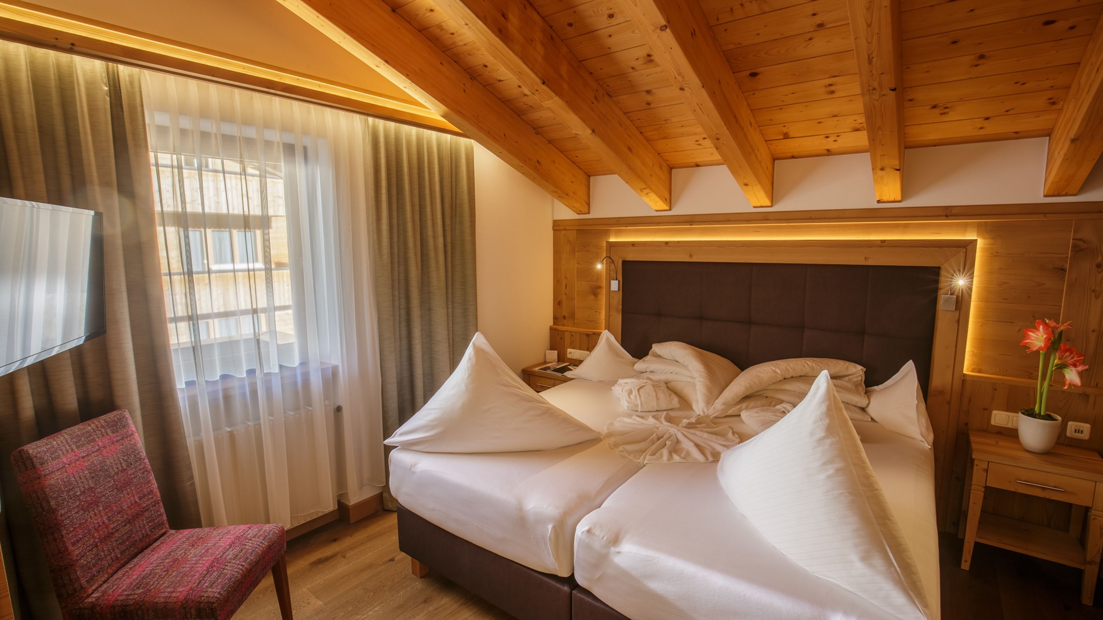 A hotel room with a large bed, wooden ceiling beams, a TV, and a chair.