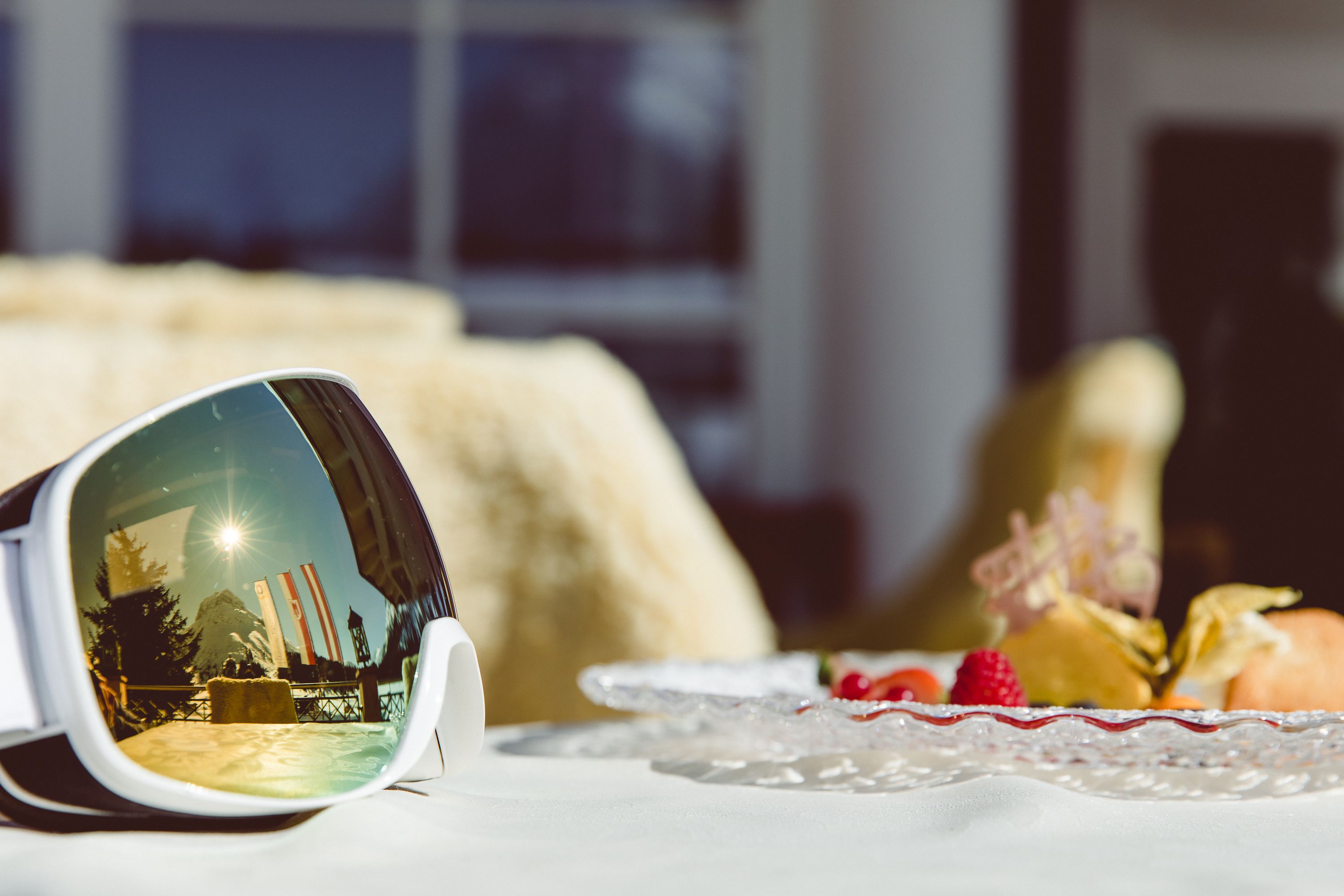 A dining table with a plate of food and a pair of sunglasses reflecting a snowy landscape.