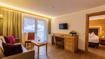 A hotel room with a wooden desk, a television, a bed, and a view of the outside.