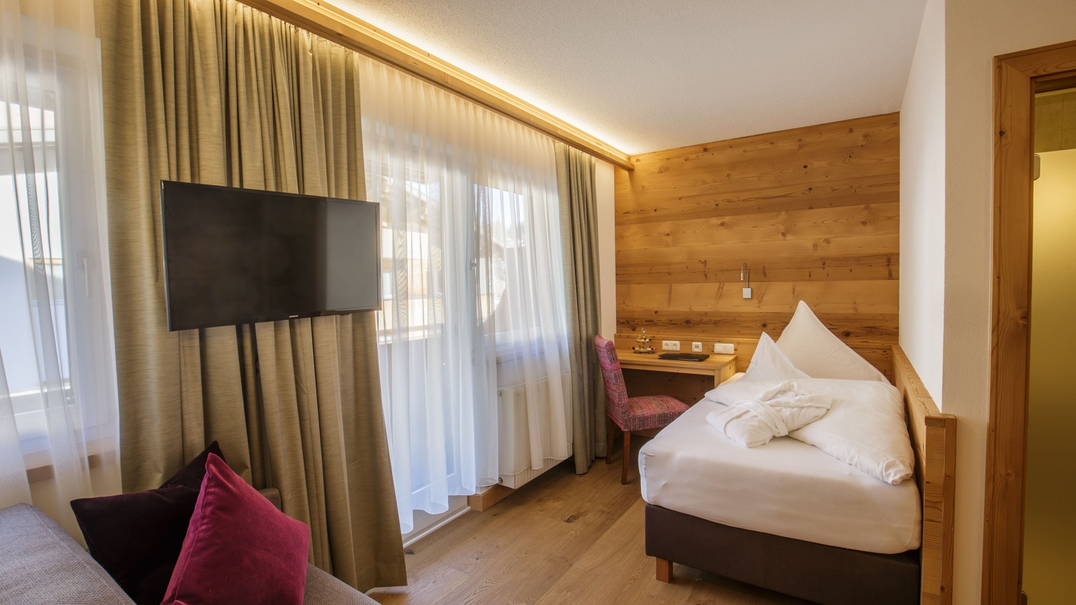 A hotel room with a bed, a desk, a chair, a television, and curtains.