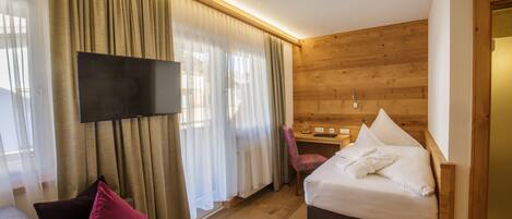 A hotel room with a bed, a desk, a chair, a television, and curtains.