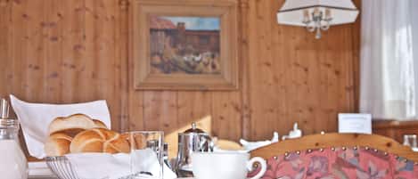 Un desayuno con pan, una taza y una tetera sobre una mesa.