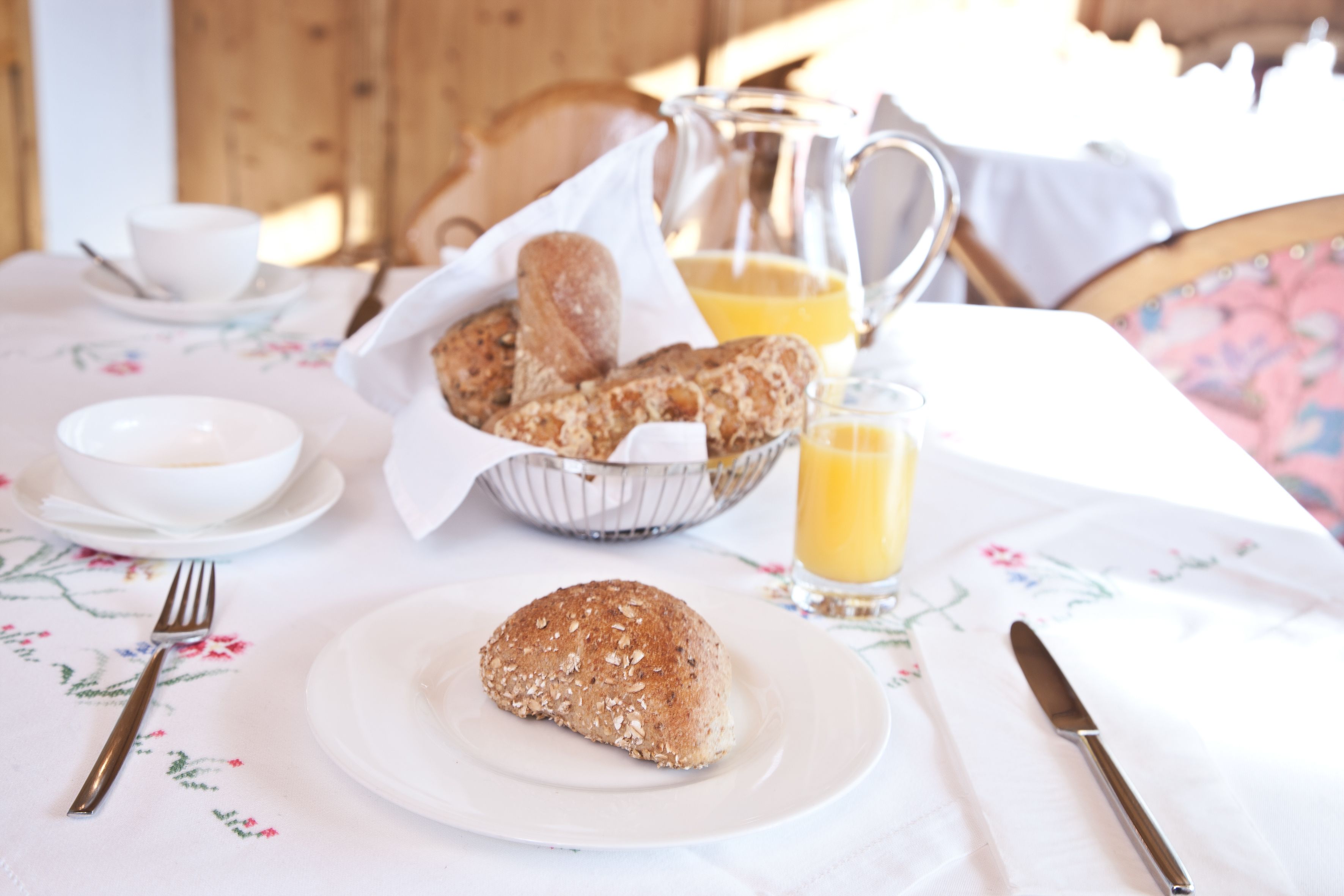 A breakfast setting with bread, a jug of orange juice, and a cup on a table.