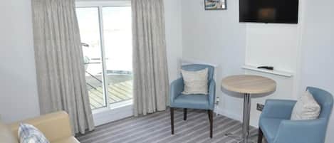 A room with a sofa, two armchairs, a small round table, a TV, and a sliding glass door leading to an outdoor area.