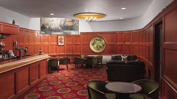 A bar area with wooden paneling, green upholstered chairs, a round table, and a red patterned carpet.