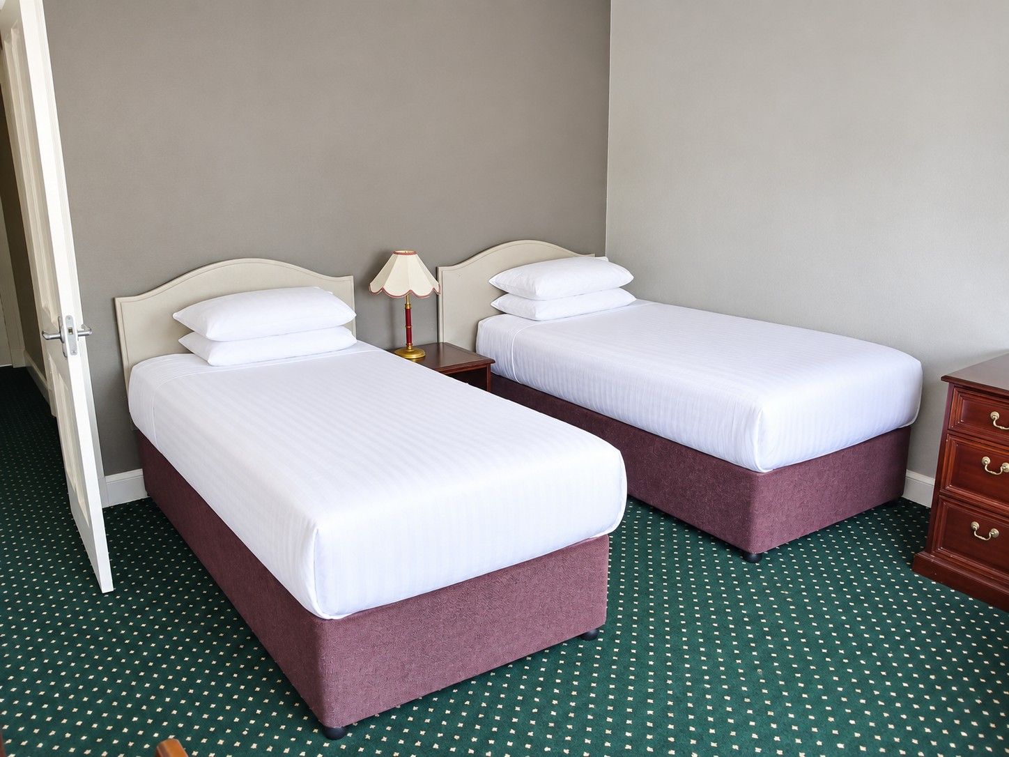 Habitación de hotel con dos camas, una mesita de noche, una lámpara y un aparador.