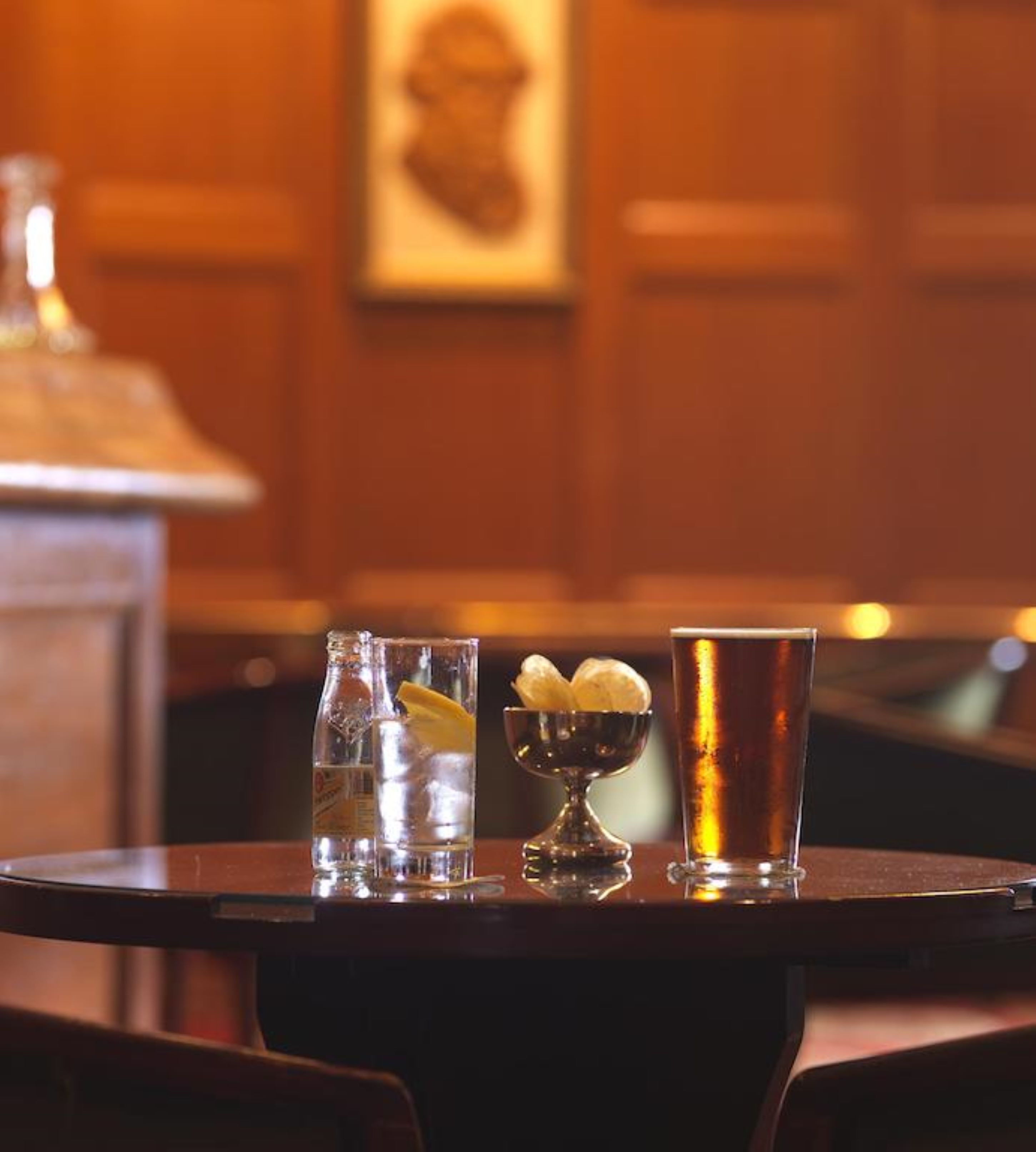 A bar area with a bottle of water, a glass with a lemon slice, and a tall glass of beer on a table.