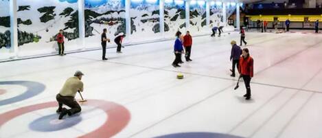Una pista de curling cubierta con varias áreas de juego y jugadores en movimiento.
