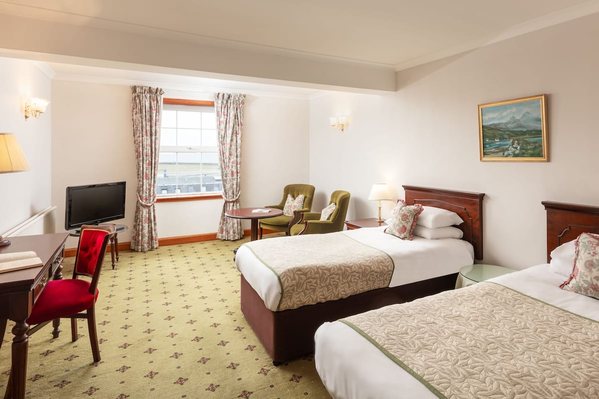 A hotel room with two beds, a desk with a chair, a television, and a window with curtains.