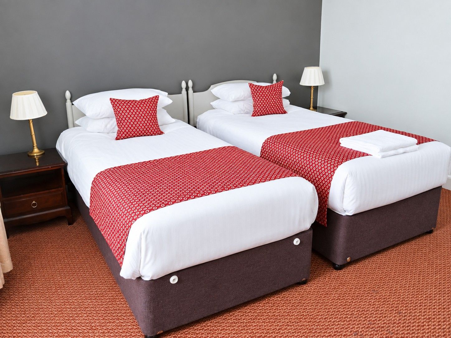 A double bed with a red and white patterned bedspread, two bedside tables with lamps, and a brown carpet.