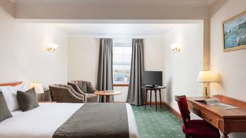 Habitación de hotel con cama, dos sillones, escritorio, televisor y ventana con cortinas.