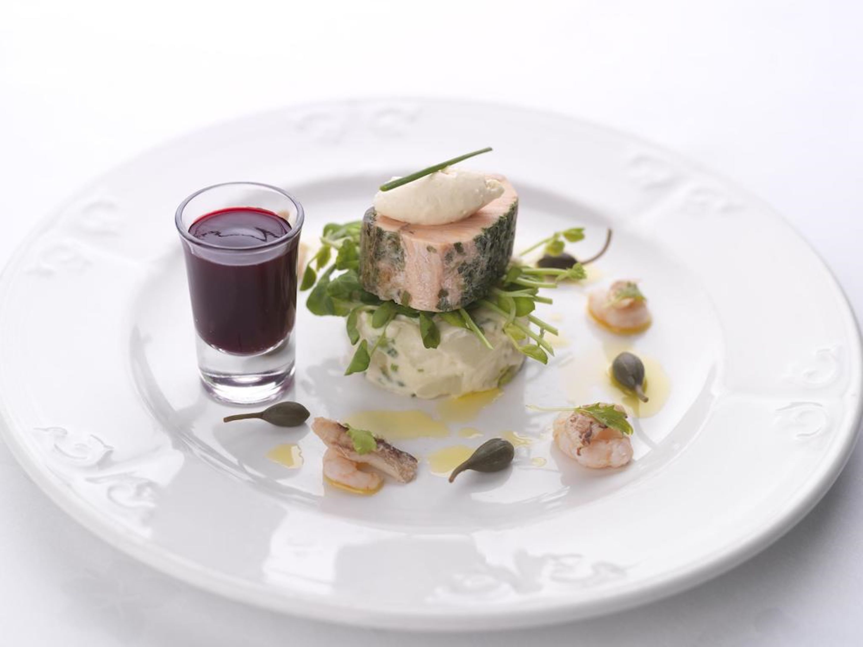 Une assiette blanche contenant un plat de fruits de mer disposés en couches, un verre de vin rouge et quelques éléments de décoration.