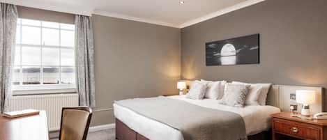 A neatly arranged bedroom with a large bed, bedside lamps, a nightstand, a chair, and a view of the outdoors through a window.