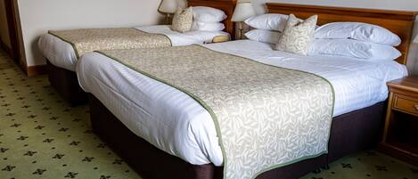 A hotel room with two beds, each with a wooden headboard, white bedding, and a green patterned carpet.