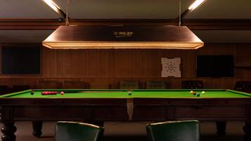 A pool table with balls, green chairs, and a ceiling light fixture.