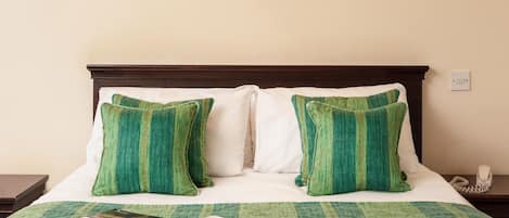 A neatly made bed with green and white bedding, a magazine on the bed, and a telephone on the nightstand.