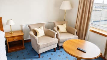 A hotel room with a bed, two armchairs, a small table, a lamp, and a view of the outside.