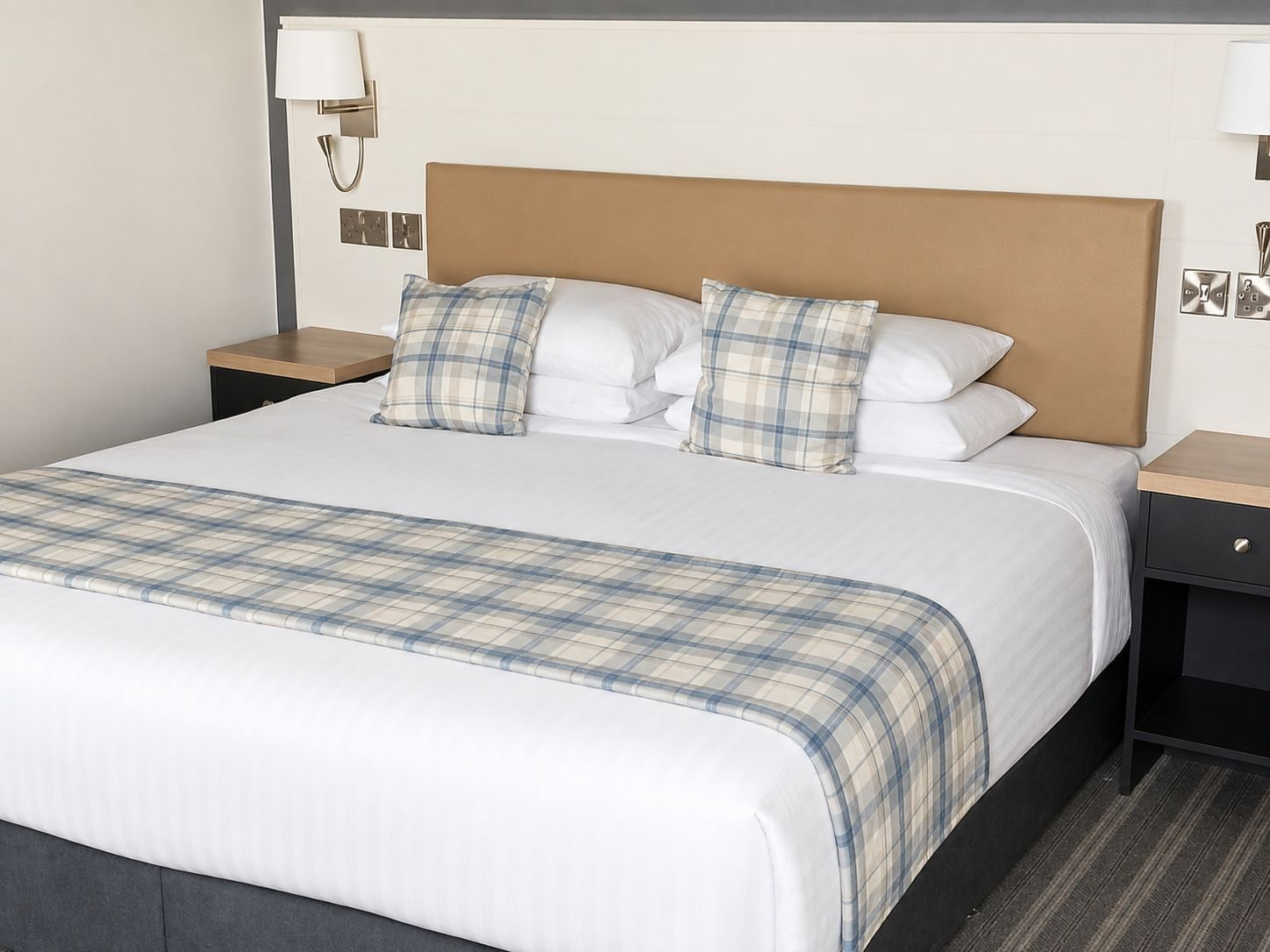 A hotel room with a large bed, two bedside tables, a headboard, and a wall-mounted lamp.