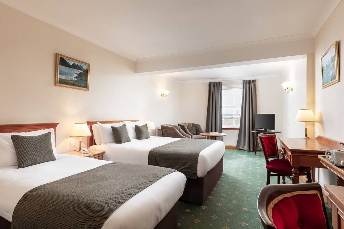A hotel room with two beds, a desk, a chair, a television, and a painting on the wall.