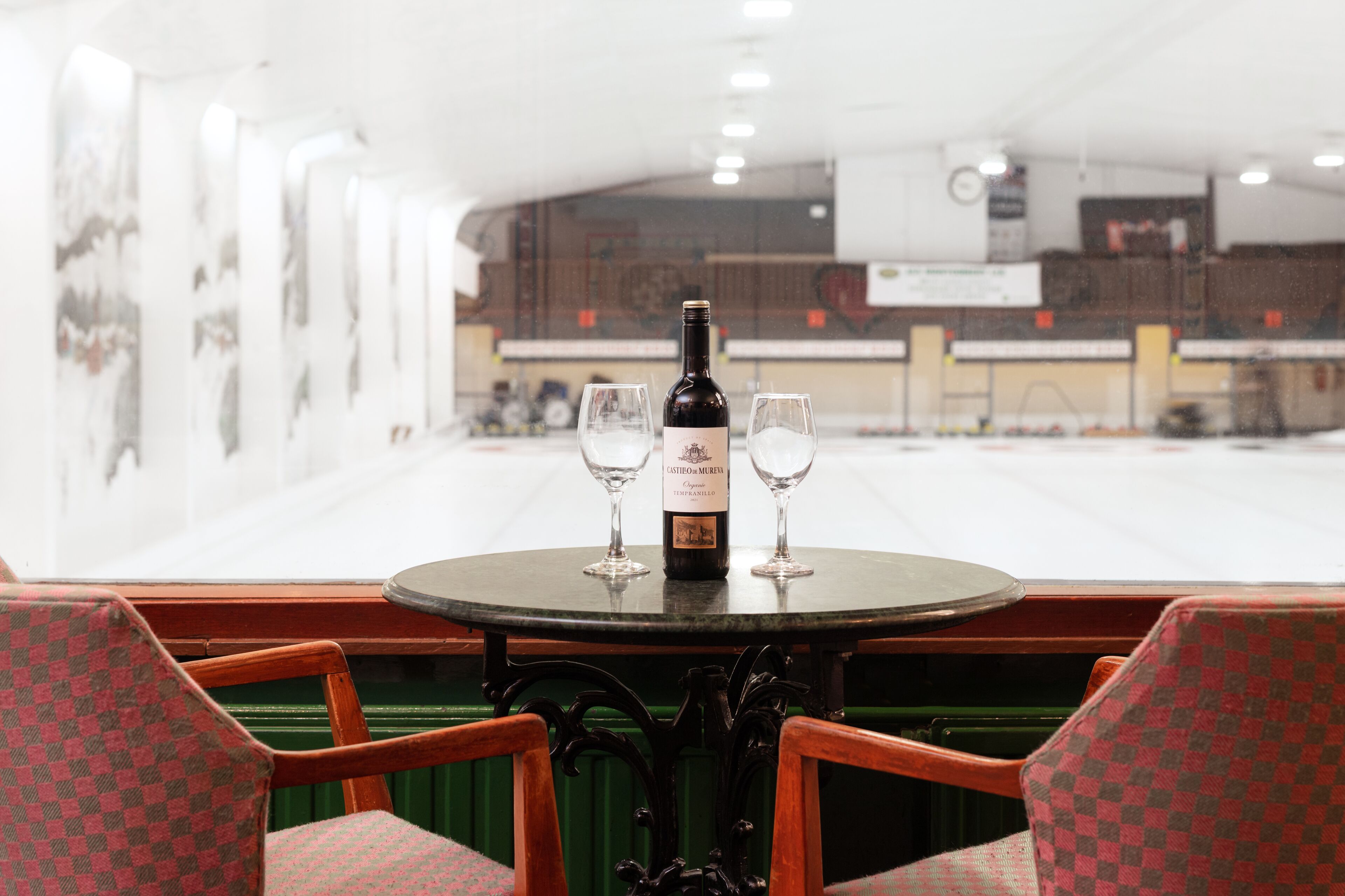 Una mesa redonda con una botella de vino y dos copas, rodeada de sillas a cuadros.