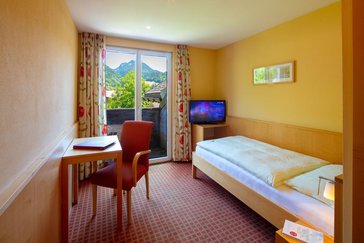 A hotel room with a bed, a desk, a chair, a television, and a window with curtains.