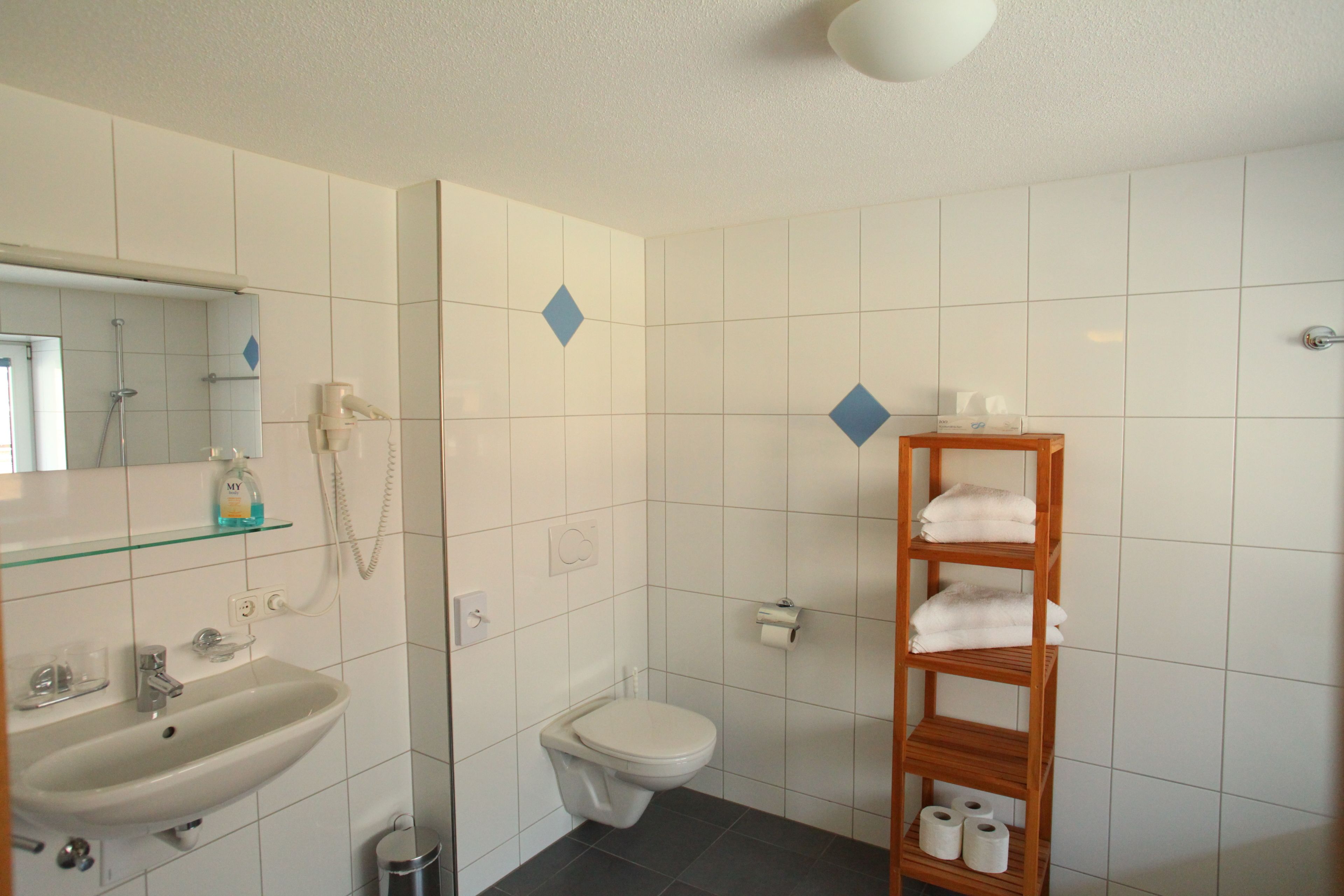 Un baño con lavamanos, inodoro y estante con toallas.