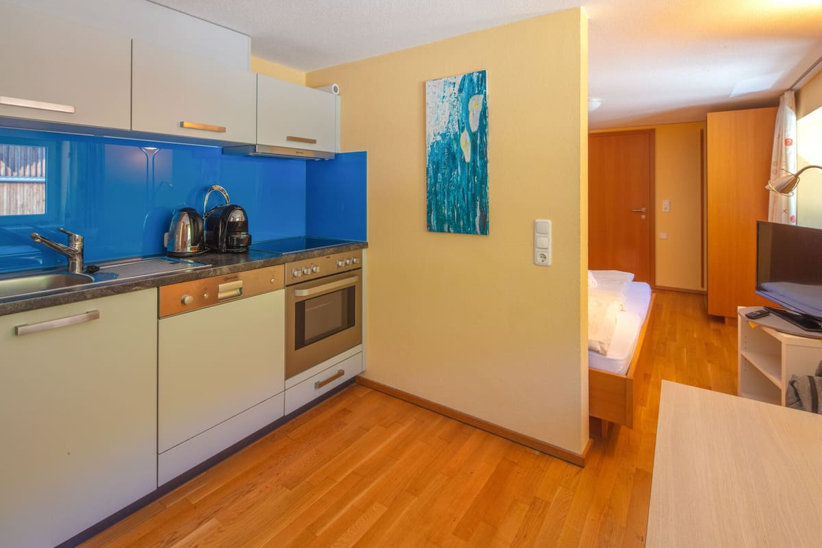 A compact kitchen with modern appliances, a dining area with a table, and a bedroom with a bed.