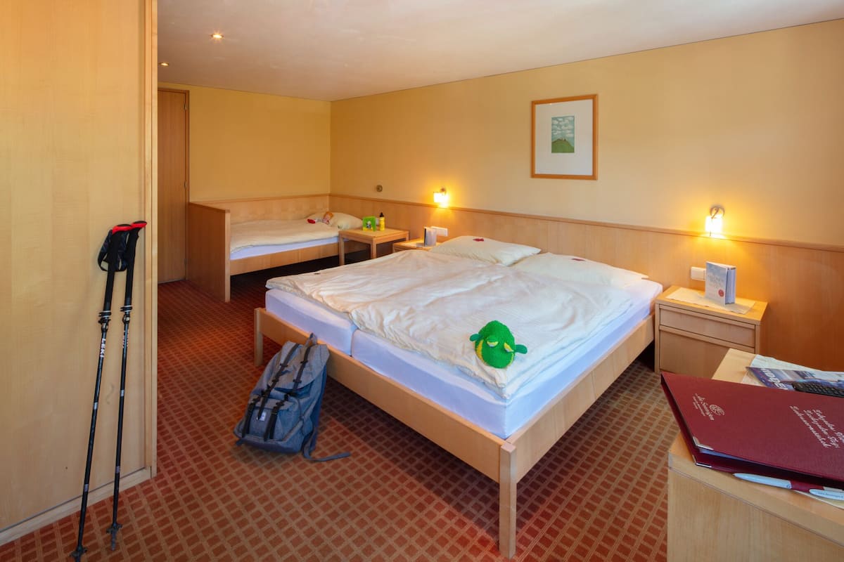 A hotel room with two single beds, a wooden nightstand, a desk with a chair, and a backpack on the floor.
