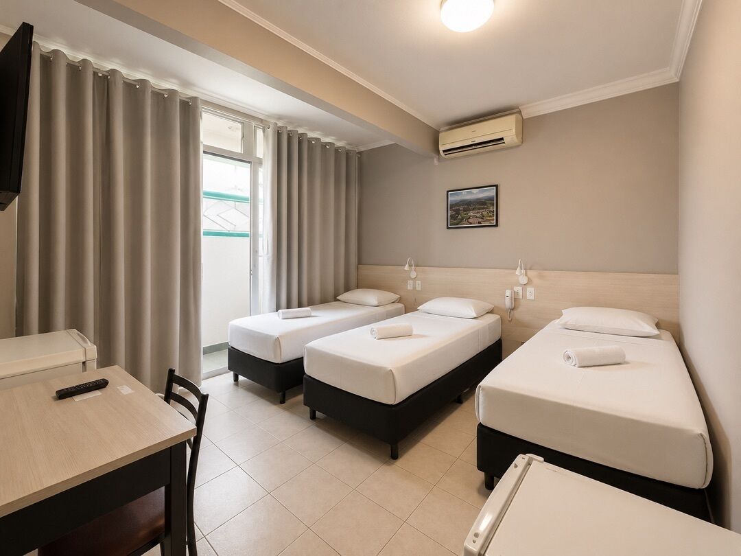 A hotel room with three beds, a desk, a chair, and a TV.