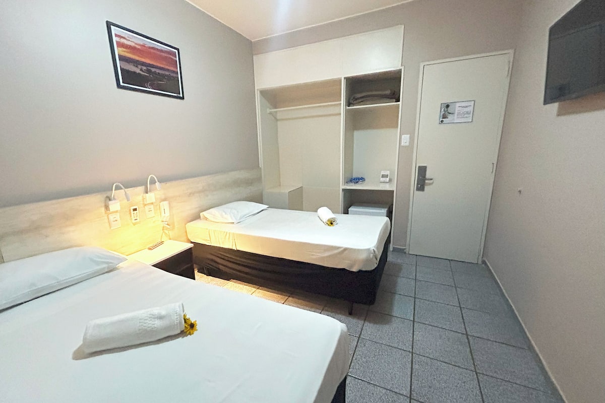 A hotel room with two beds, a wardrobe, a mirror, and a small desk with a lamp.