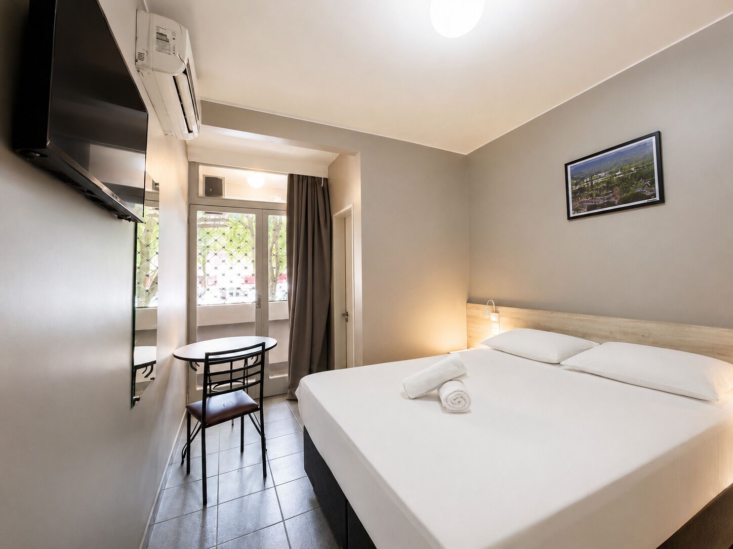Een hotelkamer met een bed, een bureau met stoel, een airconditioning en een raam met gordijnen.