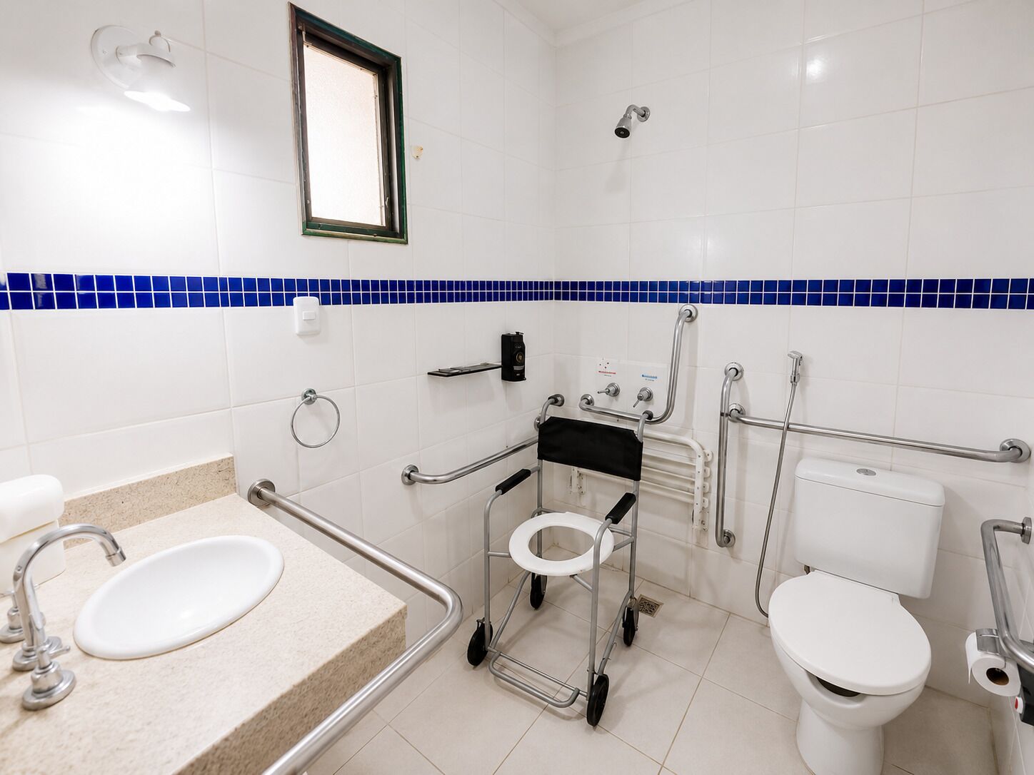 A bathroom with white tiles, a blue-tiled accent strip, a sink, a toilet, and a shower.