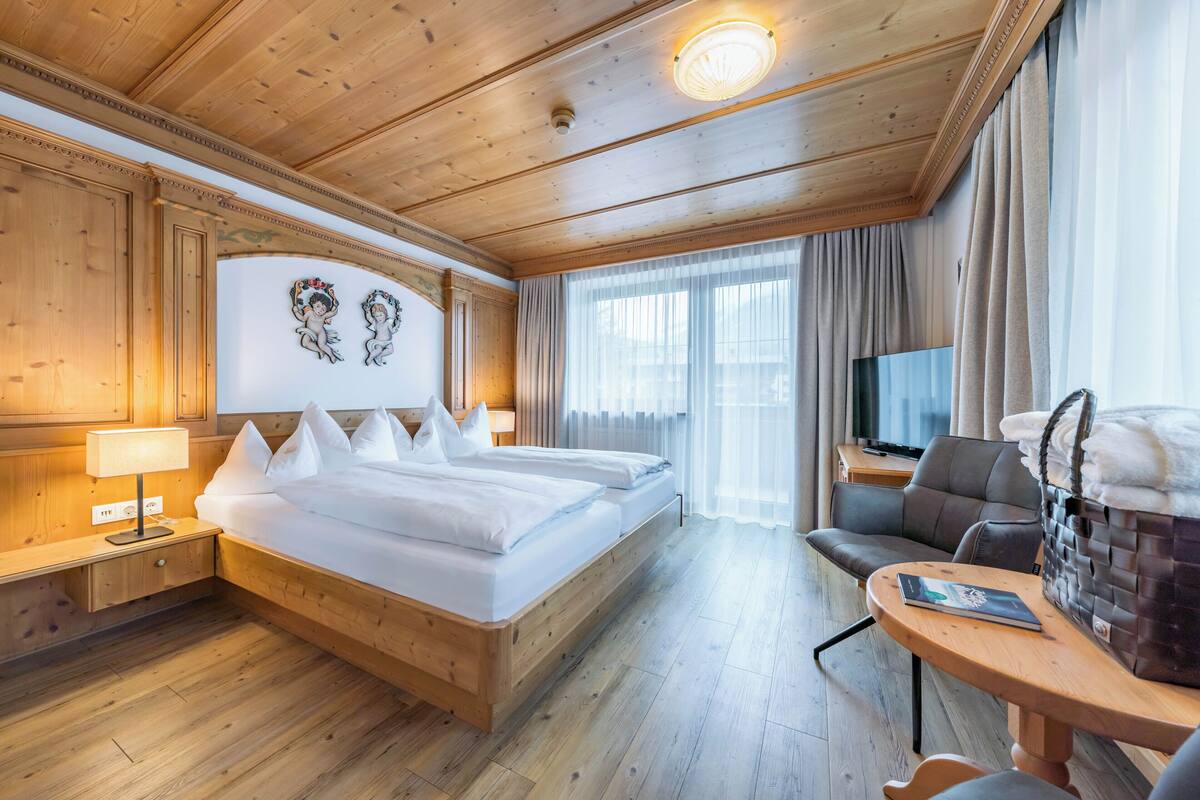 A hotel room with a wooden ceiling, two beds with white linens, a TV on a wooden table, and a window with curtains.