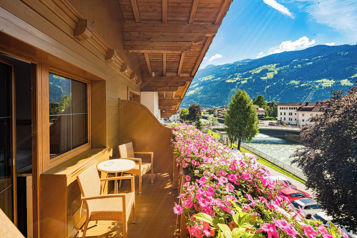 A balcony with wicker furniture, a view of a river, and mountains in the background.
