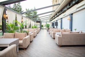 A covered outdoor seating area with beige sofas and tables, surrounded by potted plants. - GRAND HOTEL BAKU CENTRAL PARK (Baku)