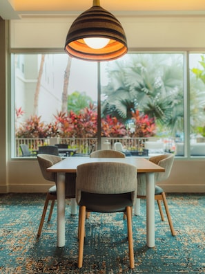 A dining area with a table and chairs, a hanging lamp, and a view of outdoor plants through large windows. - Hyatt Place Bayamon (Bayamon)