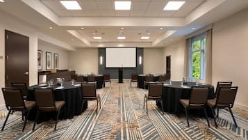 A conference room with a large screen, multiple tables, and chairs.
