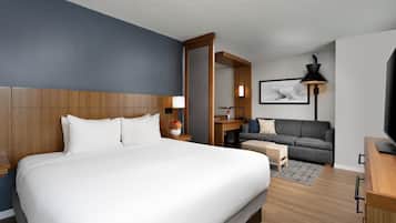 A hotel room with a large bed, a desk, a sofa, a TV, and a lamp.